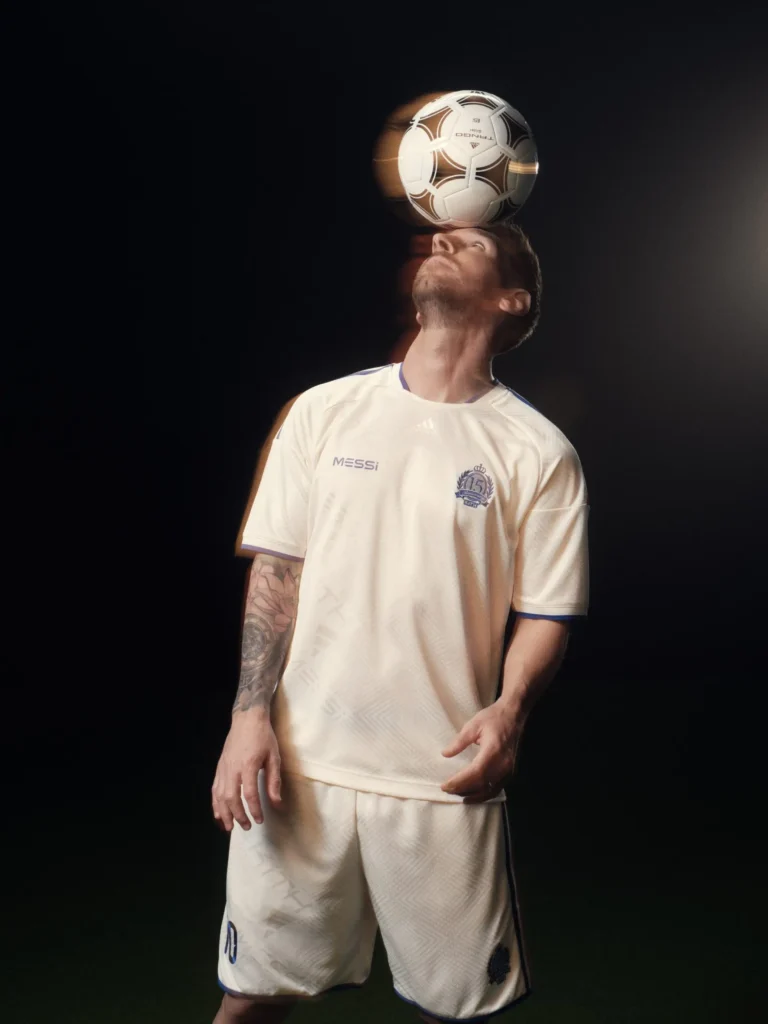 Studio action portrait of a football player balancing a football above the face while wearing a monochrome cream football kit