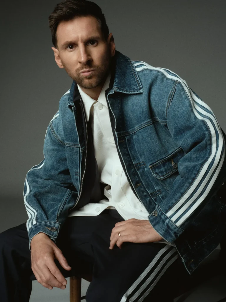 Editorial portrait of a football player seated in layered casualwear featuring a denim jacket with stripe detailing and tailored trousers