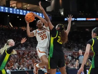 Madison Booker attacks the lane in Texas’ NCAA Tournament matchup against Oregon, elevating through multiple defenders with control and power as the Longhorns star showcases her aggressive scoring versatility under the arena lights