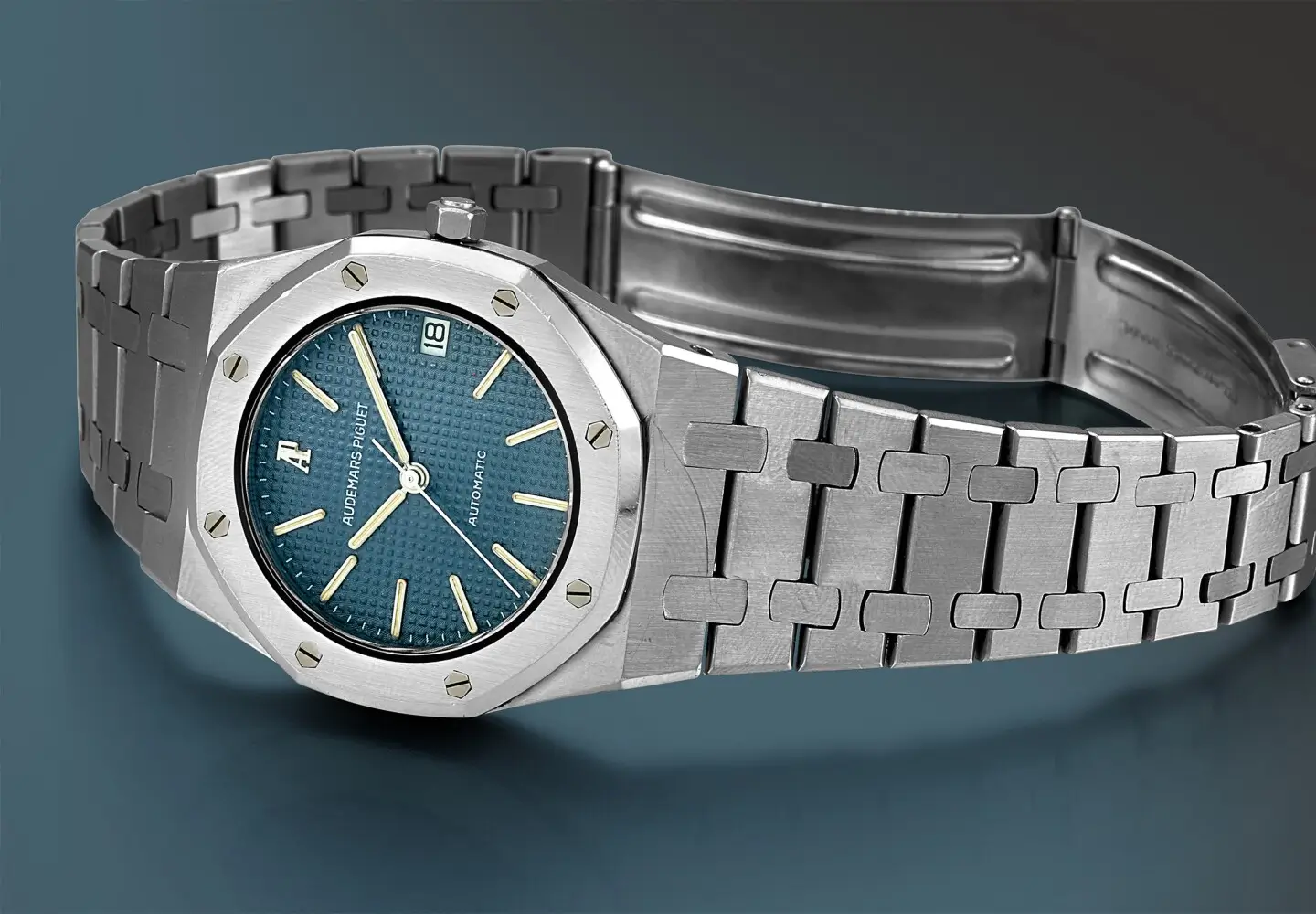 Classic Audemars Piguet Royal Oak automatic watch in stainless steel with octagonal bezel, integrated bracelet, and textured blue Tapisserie dial displayed against a dark blue background