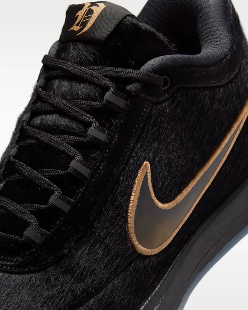 Angled close-up of the black pony hair Nike sneaker displaying tonal rope laces, bronze metallic Swoosh, gothic-inspired tongue logo, and layered premium textures