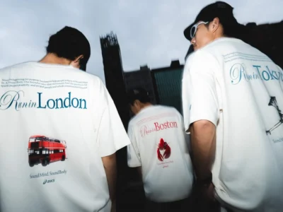 Three people walking through an urban setting wearing oversized white ASICS x P.LIFE x Worldwide Run Club graphic T-shirts featuring London, Boston, and Tokyo-inspired back prints