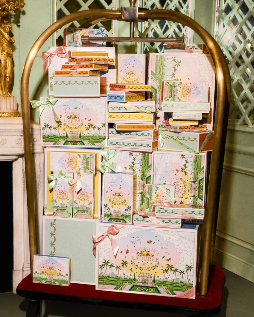 A luggage cart stacked with pastel-colored Casablanca x Ladurée gift boxes showcases the collaboration’s whimsical packaging inspired by travel, gardens, and French haute