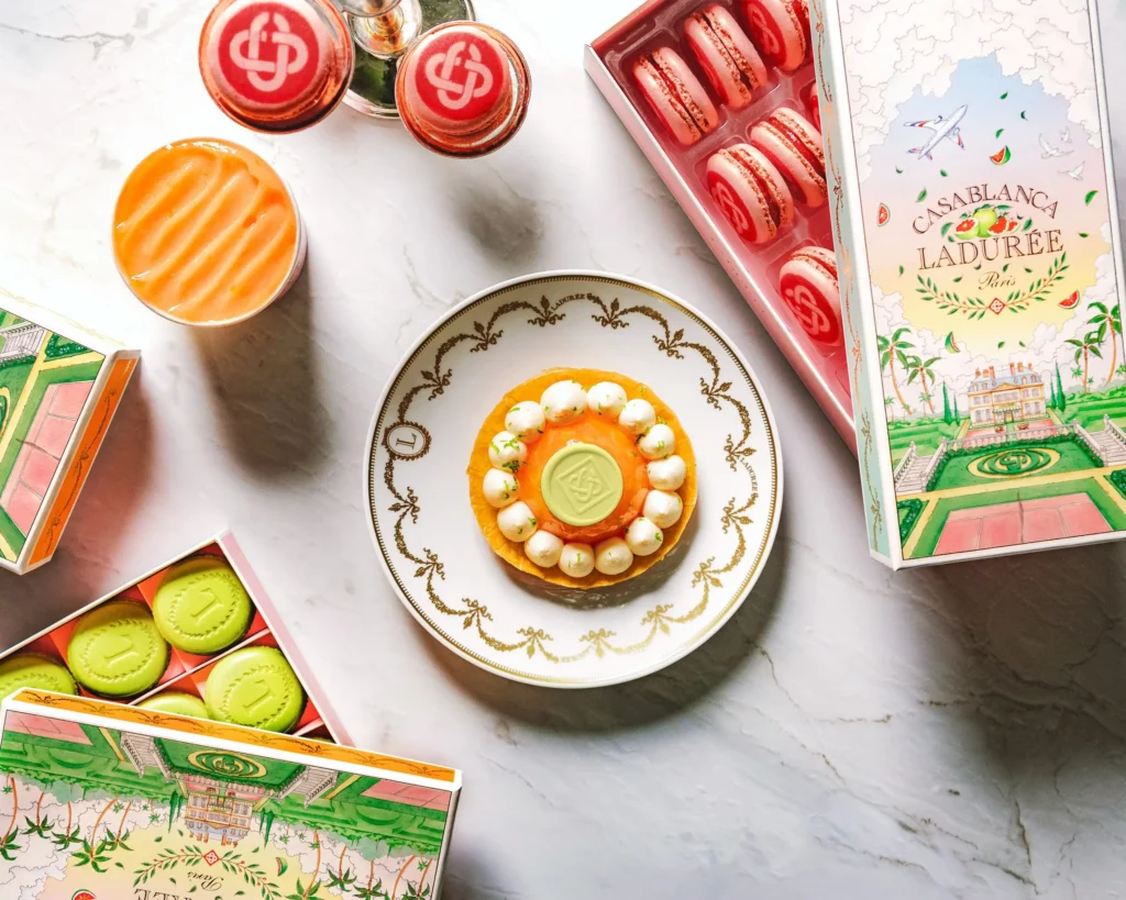 Signature Casablanca x Ladurée pastries and macarons are arranged on marble alongside collectible collaboration packaging, highlighting the collection’s vibrant pastel aesthetic and haute confectionery craftsmanship