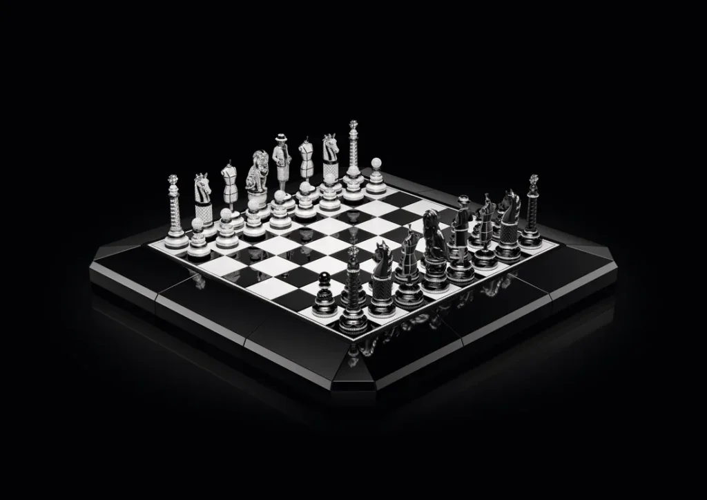 A high-luxury black-and-silver chess set displayed on a glossy elevated board against a deep black background. The sculptural pieces feature ornate detailing, including fashion-inspired figurines, horses, and architectural forms, rendered in polished metallic finishes with diamond-like embellishments. The reflective checkerboard surface and monochrome palette create a dramatic, futuristic presentation