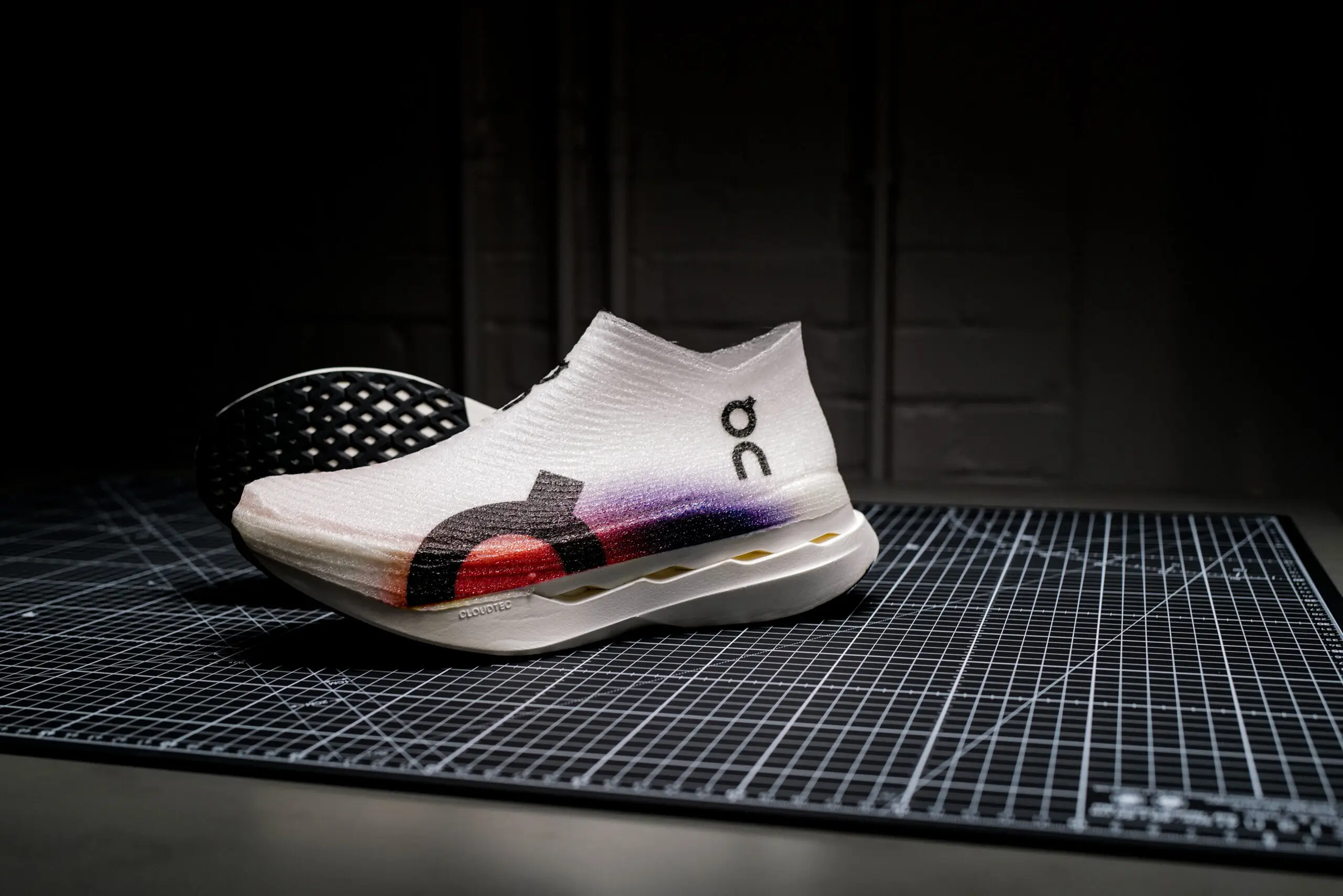 On LightSpray running shoe with a seamless, laceless white upper and subtle gradient detailing, placed on a precision cutting mat in a dimly lit studio, emphasizing the engineered texture and sculpted sole design
