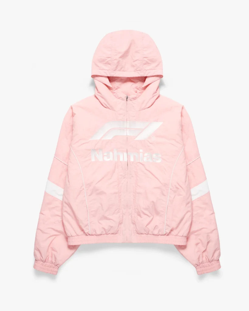 Light pink hooded zip-up jacket with a lightweight, slightly crinkled finish and a relaxed, cropped silhouette. The front features a large tonal Formula 1 logo layered above subtle “Nahmias” branding, both rendered in soft white for a low-contrast, refined effect. Reflective-style striping appears across the sleeves, complemented by curved seam lines that echo aerodynamic design cues. An adjustable hood, elasticated cuffs, and hem complete the piece, blending motorsport utility with a soft, contemporary streetwear palette