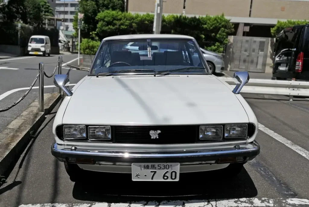 Rear passenger cabin of an Isuzu 117 Coupé featuring plush velour seating, woodgrain trim accents, and a luxurious 2+2 interior designed for comfortable long-distance touring