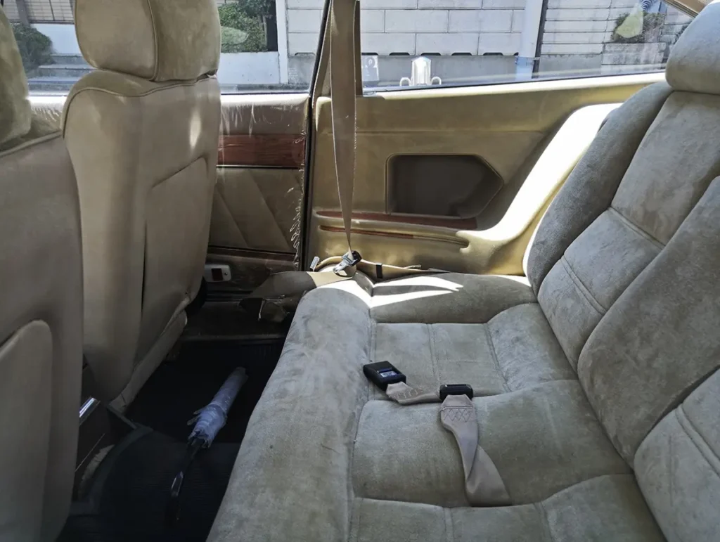 Rear passenger cabin of an Isuzu 117 Coupé featuring plush velour seating, woodgrain trim accents, and a luxurious 2+2 interior designed for comfortable long-distance tour