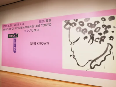 Wide installation view of the (UN)KNOWN HIROKO KOSHINO – New Theory / True Theory exhibition entrance wall at the Museum of Contemporary Art Tokyo, featuring a large soft pink graphic panel with exhibition dates, bilingual Japanese and English typography, Hiroko Koshino branding, and an expressive black ink portrait illustration displayed across the gallery space