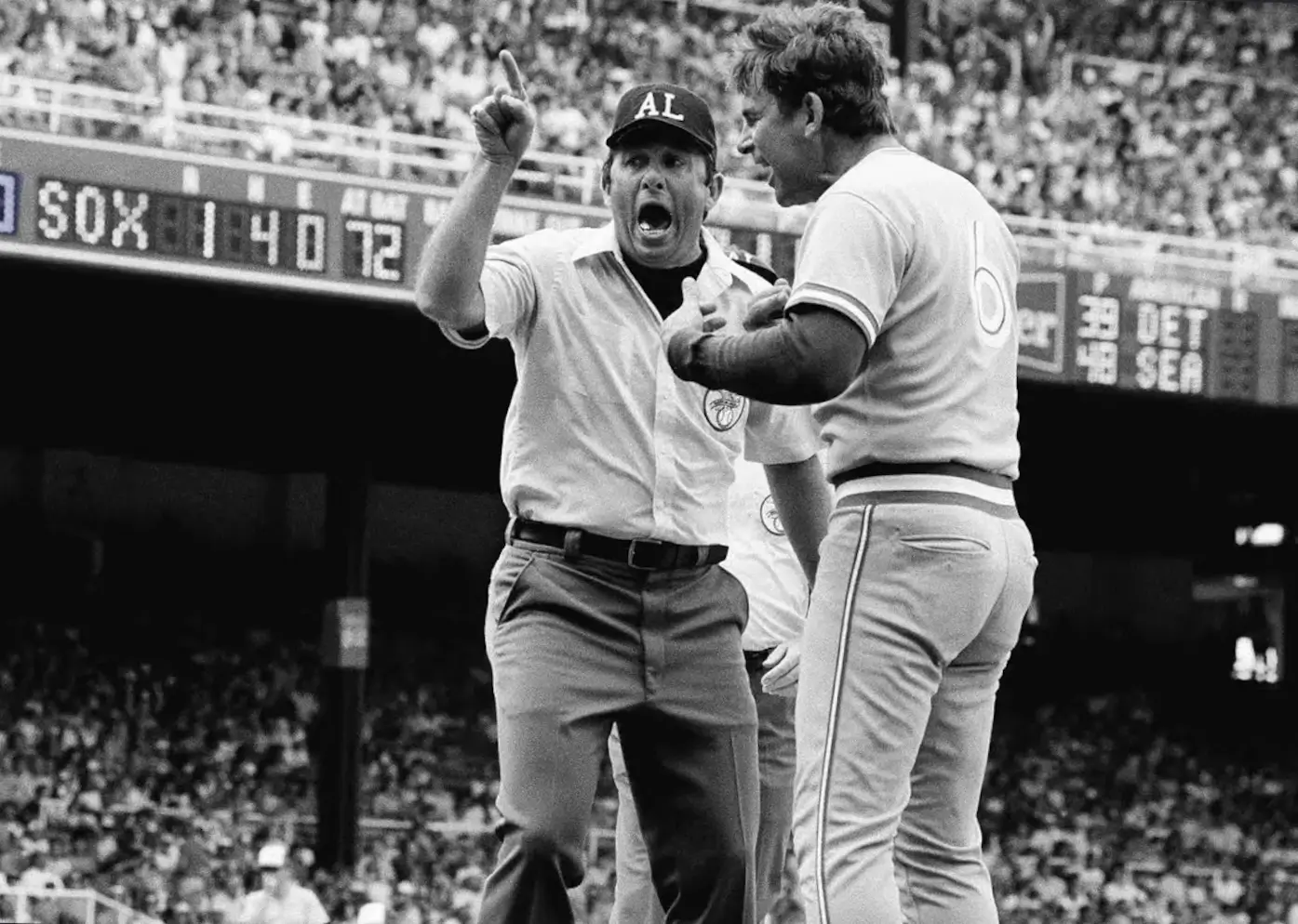 Black-and-white archival photo of Bobby Cox passionately arguing with an umpire during a baseball game, capturing the fiery competitiveness that became synonymous with his managerial career. Surrounded by a packed stadium crowd, the moment reflects Cox’s fierce loyalty to his players and his legendary on-field intensity