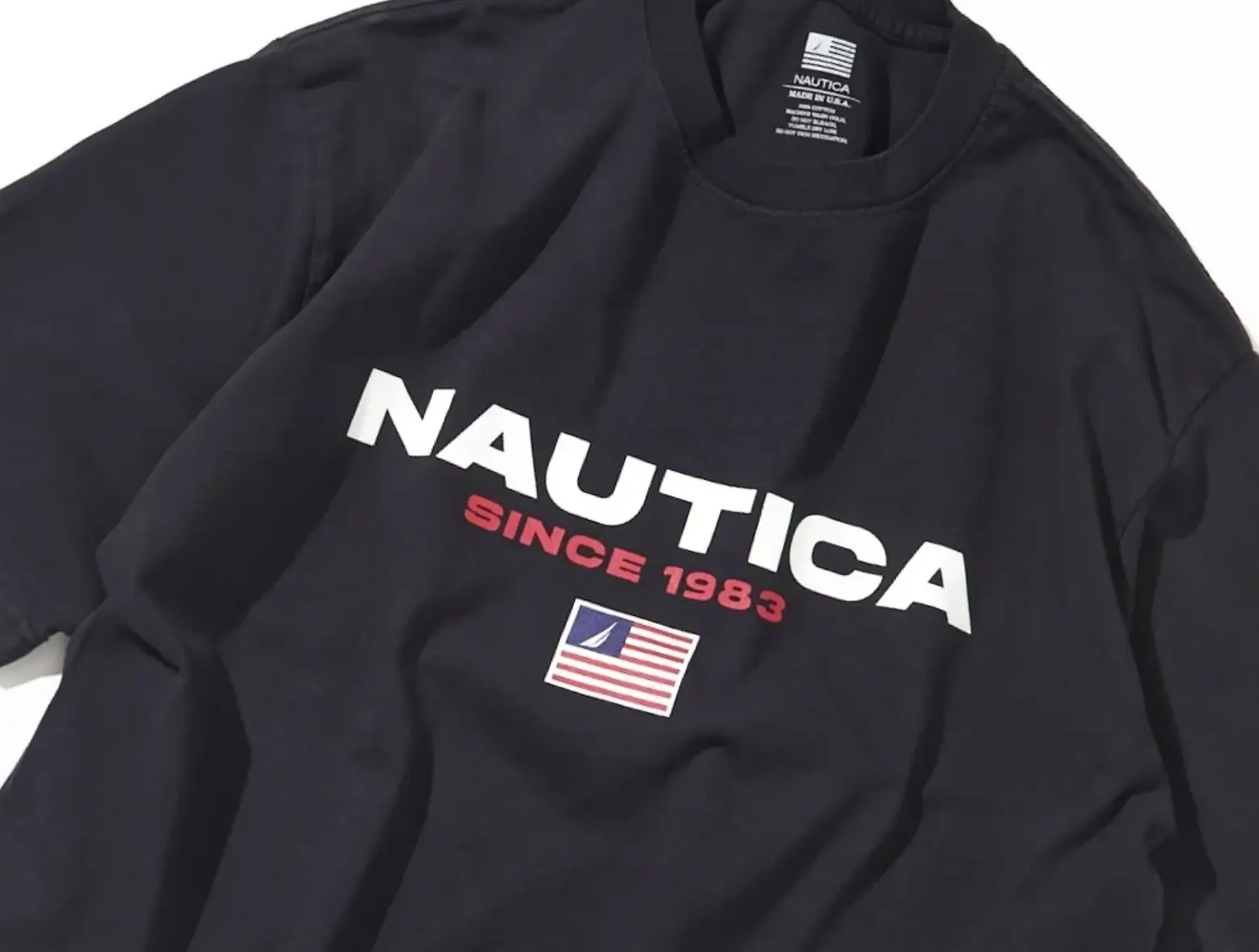 Close-up of a navy Nautica Made in USA oversized graphic T-shirt featuring bold white Nautica logo lettering, red “Since 1983” text, signature heritage flag graphic, and heavyweight vintage-inspired cotton construction