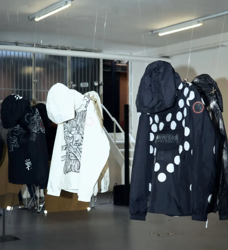 Suspended Napapijri ANORAK REFORGED outerwear installations displayed in an industrial gallery setting, featuring graphic prints, oversized hoods, and sculptural reinterpretations during Milan Design Week 2026