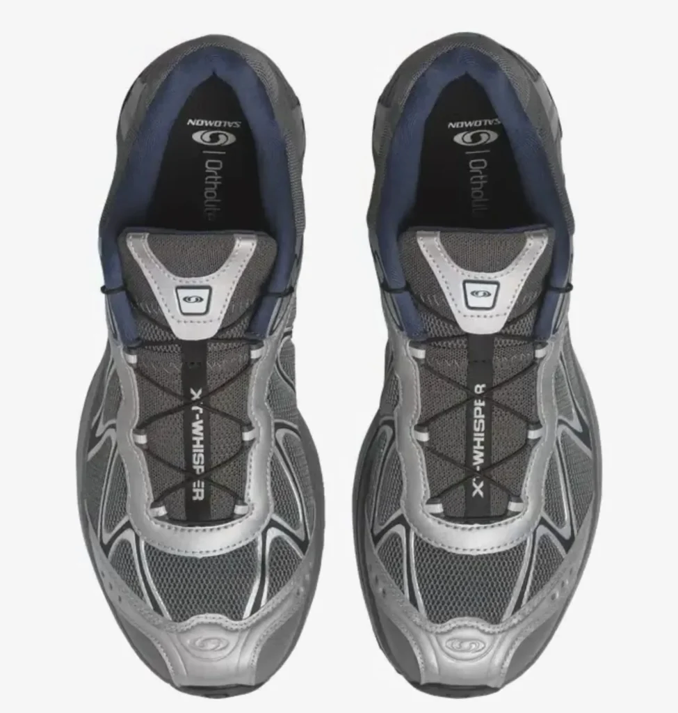 Top-down view of the Salomon XT-Whisper sneakers in grey and silver, showing breathable mesh uppers, layered synthetic overlays, and the Quicklace system across the tongue, with “XT-Whisper” branding visible and padded navy collars framing the OrthoLite® footbeds