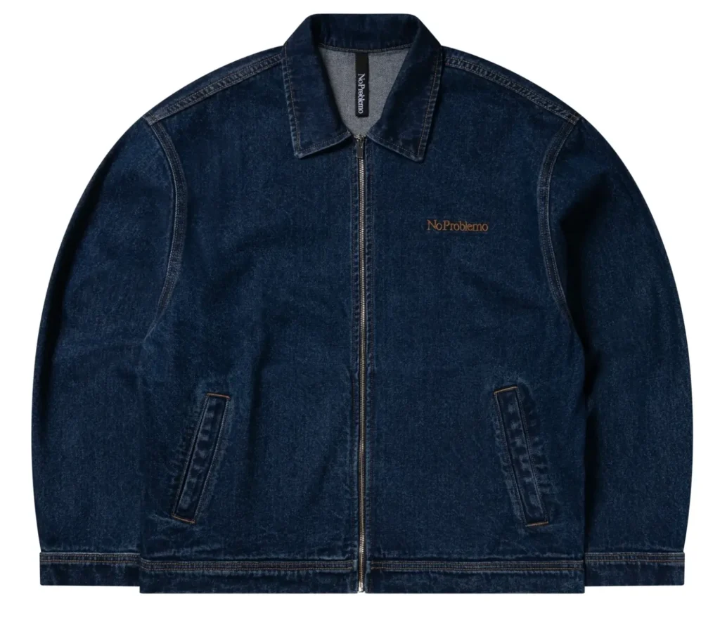 Dark indigo denim zip-up jacket with a clean minimalist silhouette, featuring subtle “No Problemo” embroidery on the chest, contrast stitching, and angled front pockets in a studio