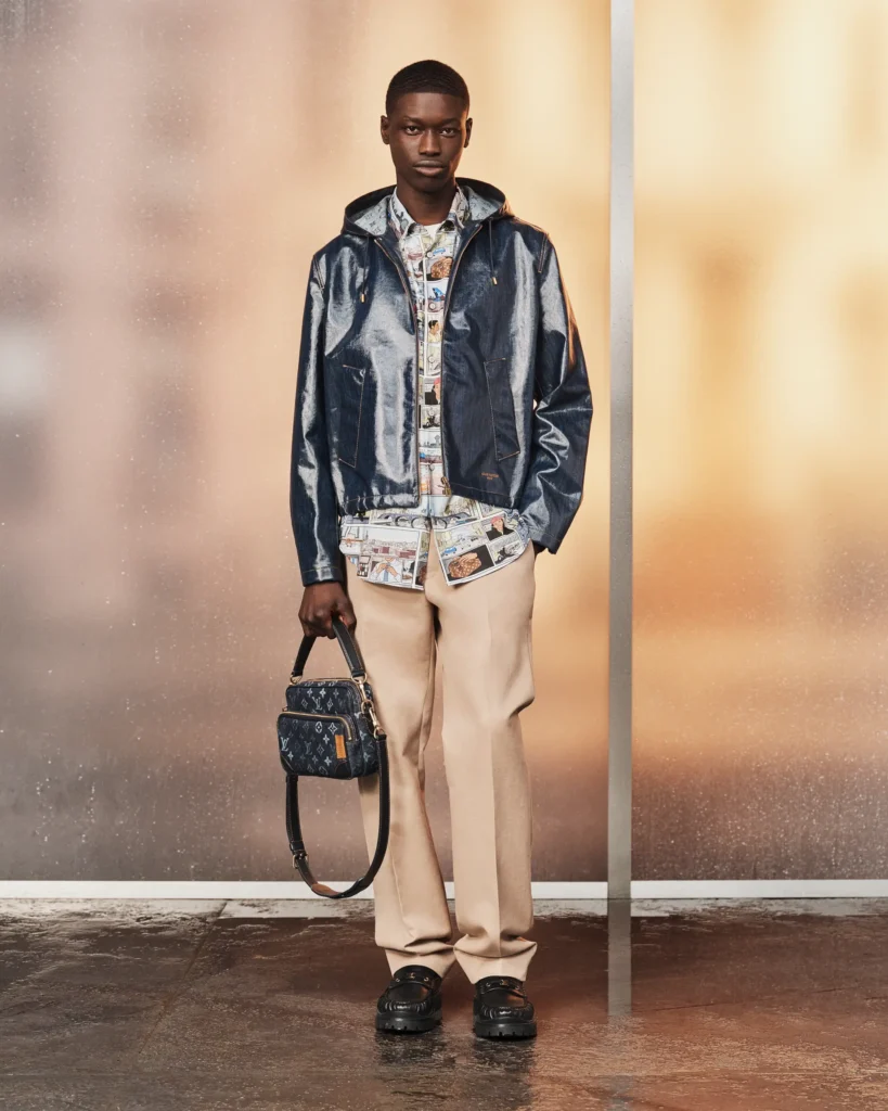 Glossy navy hooded jacket paired with a comic-print shirt, beige trousers, and a compact Louis Vuitton monogram crossbody bag