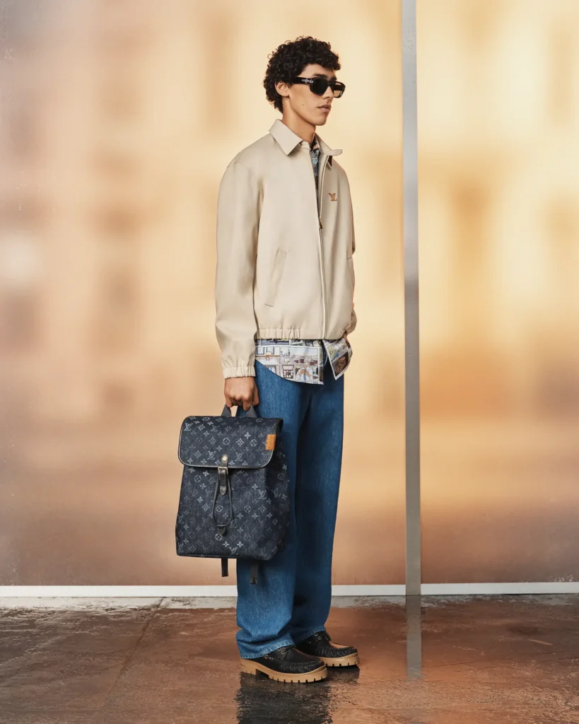 Louis Vuitton Pre-Collection Spring/Summer 2027 look featuring a navy quarter-zip sweater, relaxed beige trousers, hiking-inspired boots, and a branded shopping tote