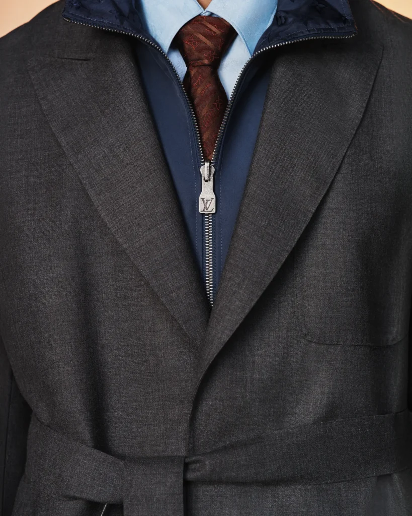 Close-up detail of a gray belted suit layered over a navy zip-front shirt and burgundy patterned tie with Louis Vuitton hardware