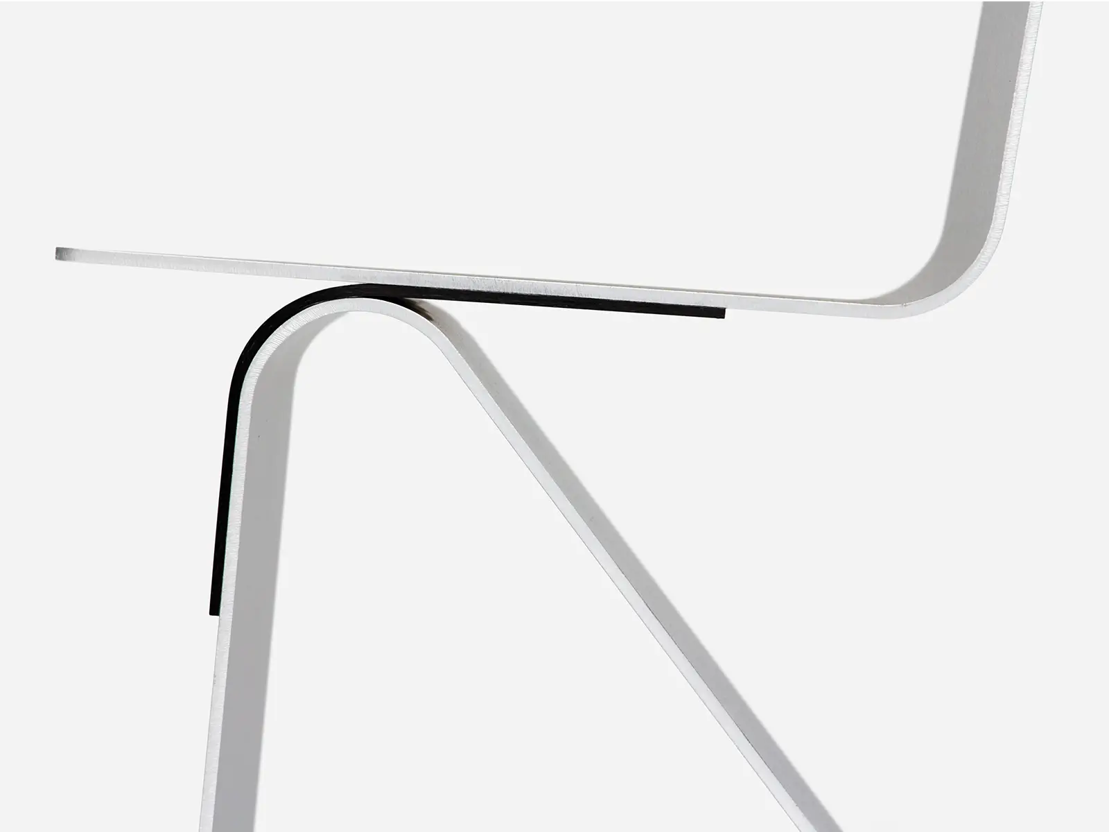 Close-up architectural detail of Leon Ransmeier’s Aluminum Chair, highlighting the brushed aluminum frame, curved structural bend, and exposed carbon fiber composite joint against a minimalist studio backdrop