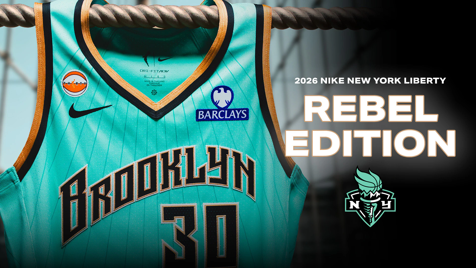 image of the 2026 Nike New York Liberty Rebel Edition WNBA jersey in bright turquoise with gold and black trim, hanging over a thick industrial cable beside bold “Rebel Edition” typography and the Liberty torch logo against a dark urban-inspired backdrop