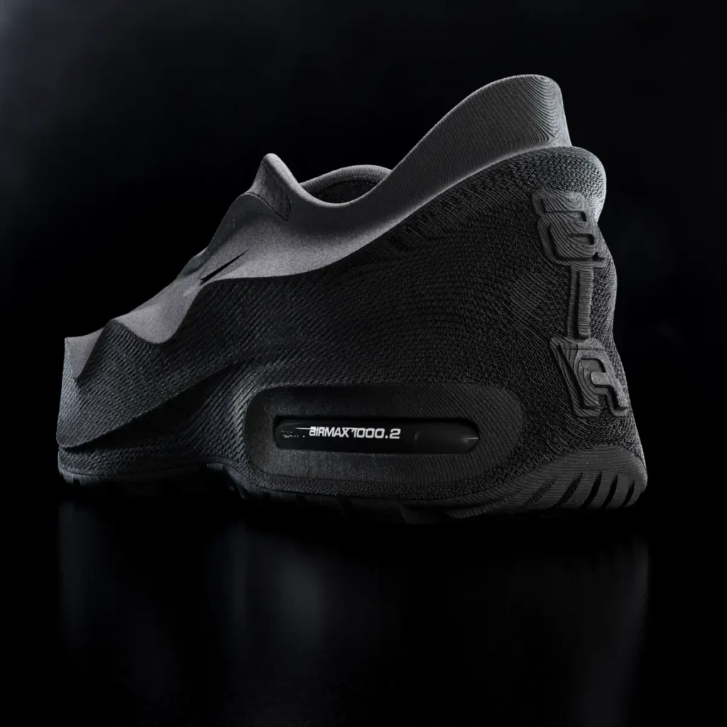 Rear-angle view of an all-black futuristic Nike Air Max 1000.2 shoe with sculpted textured heel, visible Air unit, and molded slip-on construction against a dark studio background