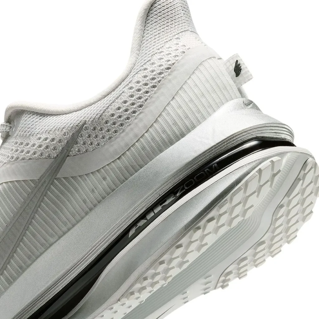 Close-up detail of a white performance shoe highlighting its sculpted midsole construction, breathable engineered mesh upper, tonal layered overlays, and a visible black Zoom cushioning unit integrated through the heel and midfoot. The outsole features a geometric traction pattern, emphasizing lightweight running functionality and a futuristic monochrome finish