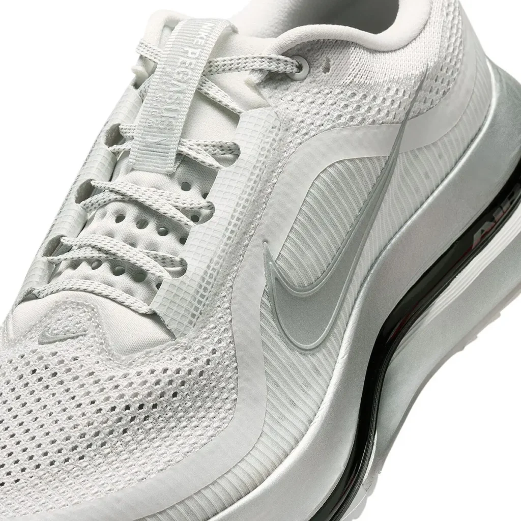 Close-up angled detail of the white Nike Pegasus Premium running shoe highlighting its breathable open-knit mesh forefoot, perforated lace shroud construction, tonal woven laces, and elongated metallic silver Swoosh overlay. The sculpted foam midsole frames a visible black Air Zoom cushioning unit, emphasizing the model’s lightweight engineering and elevated performance aesthetic