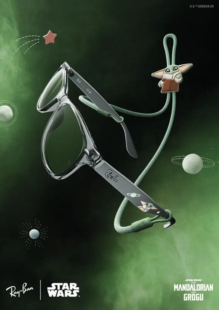 A translucent grey-green pair from the Ray-Ban x Star Wars: The Mandalorian and Grogu collaboration floats through a luminous emerald galaxy backdrop, combining sleek contemporary eyewear design with play character-driven detailing. The semi-transparent frames are paired with dark green-tinted lenses and accented by illustrated Grogu graphics along the temples, while a matching green eyewear cord features an attached Grogu charm that enhances the collectible, toy-like atmosphere of the release. Suspended among illustrated planets and cosmic doodles, the sunglasses channel a softer, more whimsical interpretation of sci-fi luxury — blending Ray-Ban’s fashion heritage with the childlike wonder and interstellar identity of the Star Wars universe