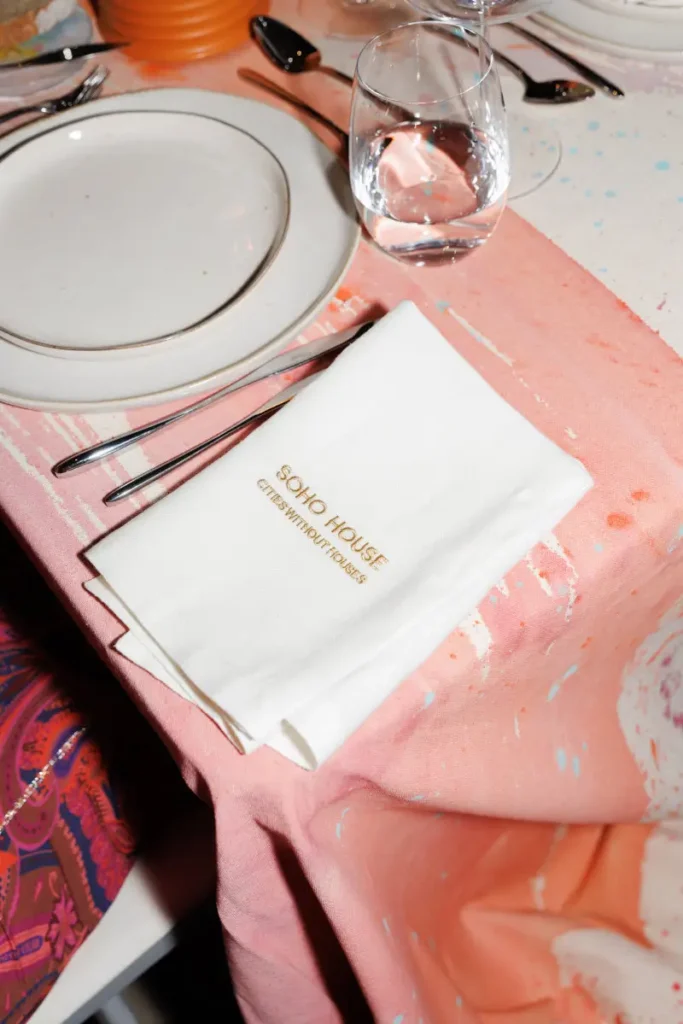Guests gathered around an art-covered dining table as wine is poured beside LOEWE candles and custom-painted surfaces during the immersive Soho House Lisbon dinner experience