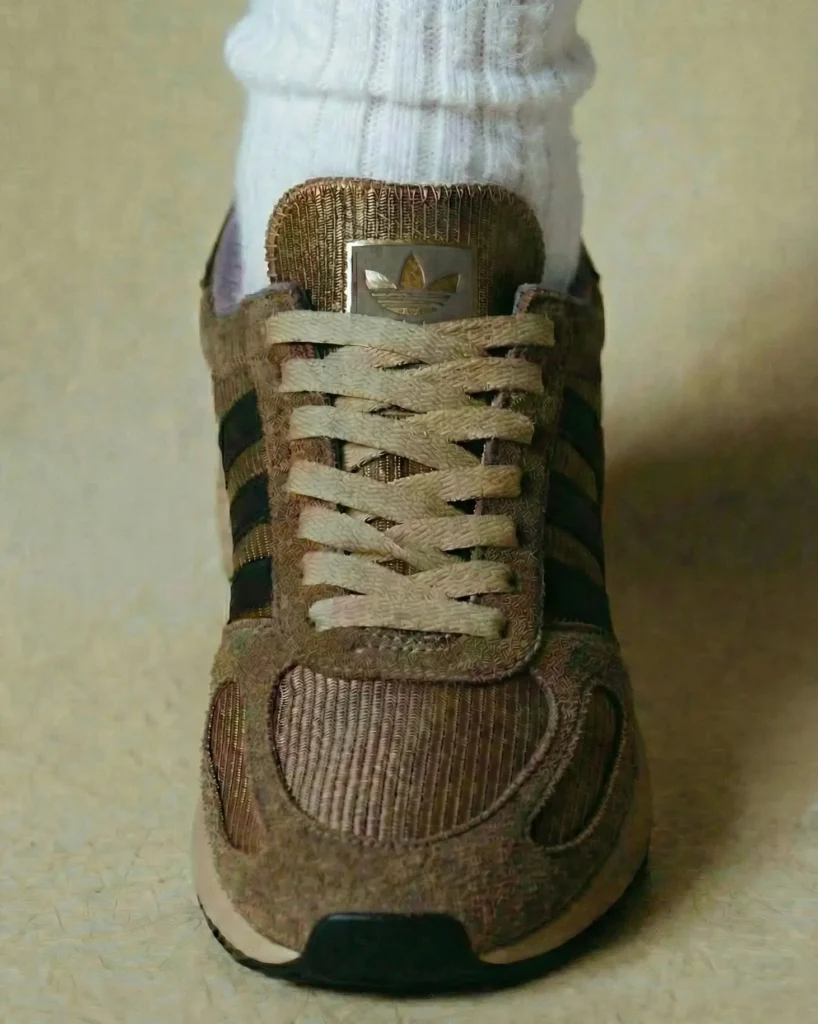 A close-up frontal view captures the adidas L.A. Trainer worn with ribbed white socks, highlighting the sneaker’s brown suede overlays, textured mesh base, tonal laces, and classic Three Stripes branding through a soft vintage-inspired editorial aesthetic