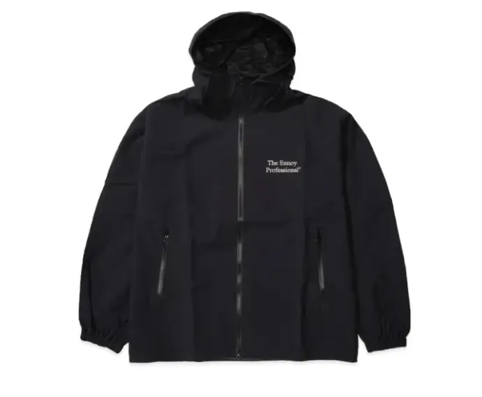 The Ennoy Professional® black technical hooded jacket featuring a minimalist zip-front construction, subtle white chest logo, and concealed utility detailing. Designed with clean lines, lightweight weather-resistant styling, and understated proportions, the piece captures Ennoy’s signature approach to functional Japanese outerwear and quiet everyday hush