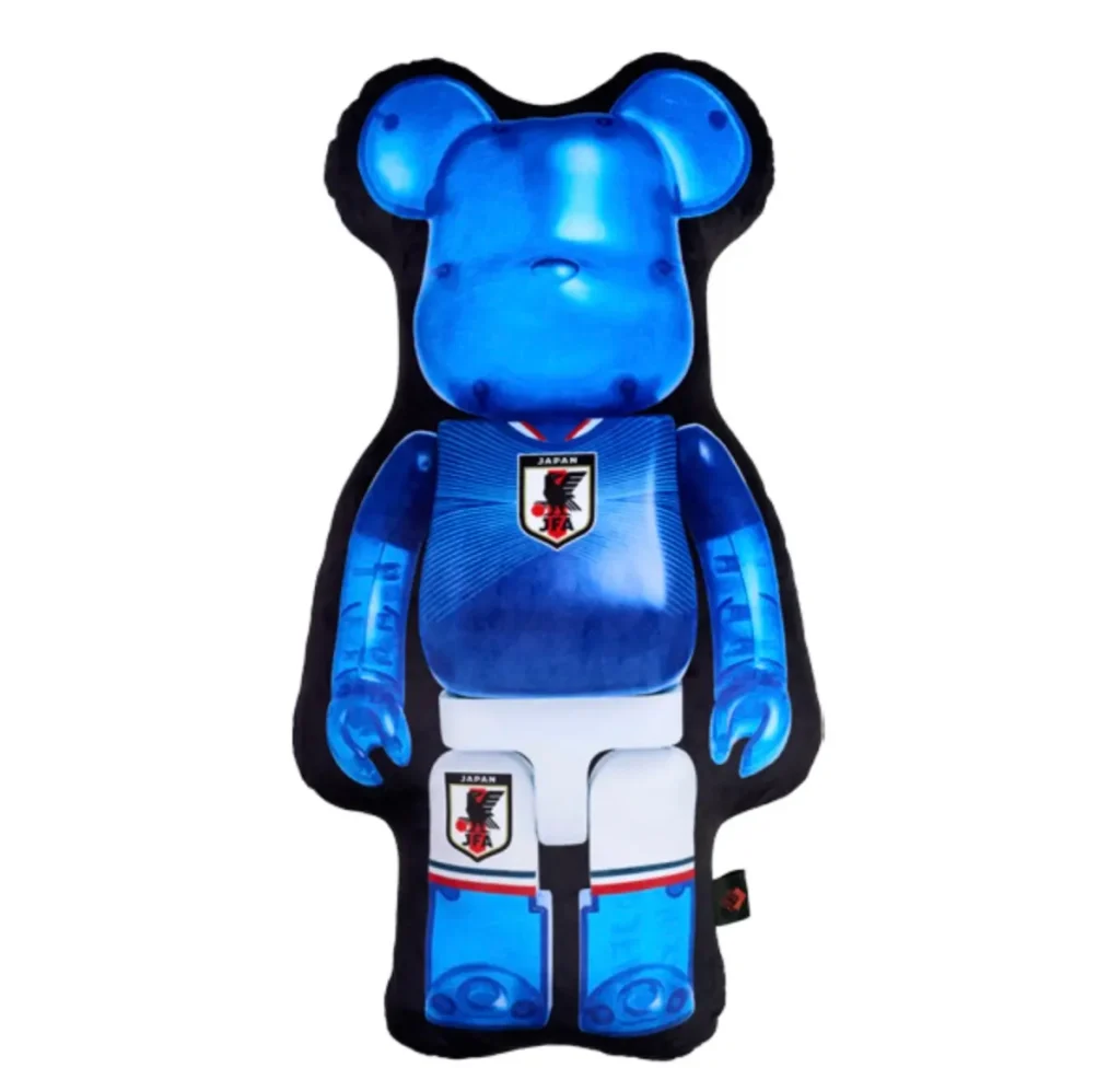Official BE@RBRICK × Japan National Soccer Team (SAMURAI BLUE) cushion designed in the silhouette of the collectible bear figure, featuring translucent blue character artwork, Japan’s national football jersey graphics, the JFA crest, and a plush oversized format for display or lounge use