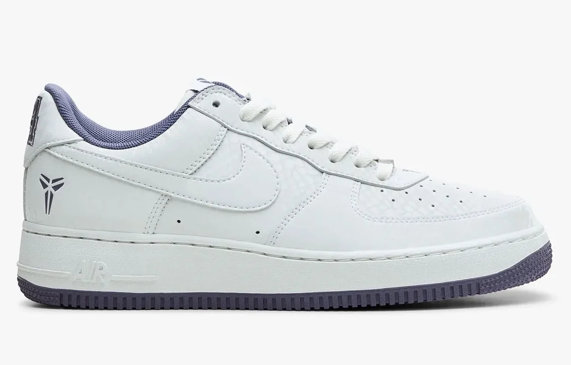 Studio side-profile image of the Nike Kobe Air Force 1 Low “Daybreak” featuring a clean white leather upper with subtle textured paneling, tonal Swoosh branding, soft lavender collar lining and outsole accents, and Kobe’s signature sheath logo printed near the heel. The minimalist palette highlights the sneaker’s refined tribute aesthetic and everyday wear