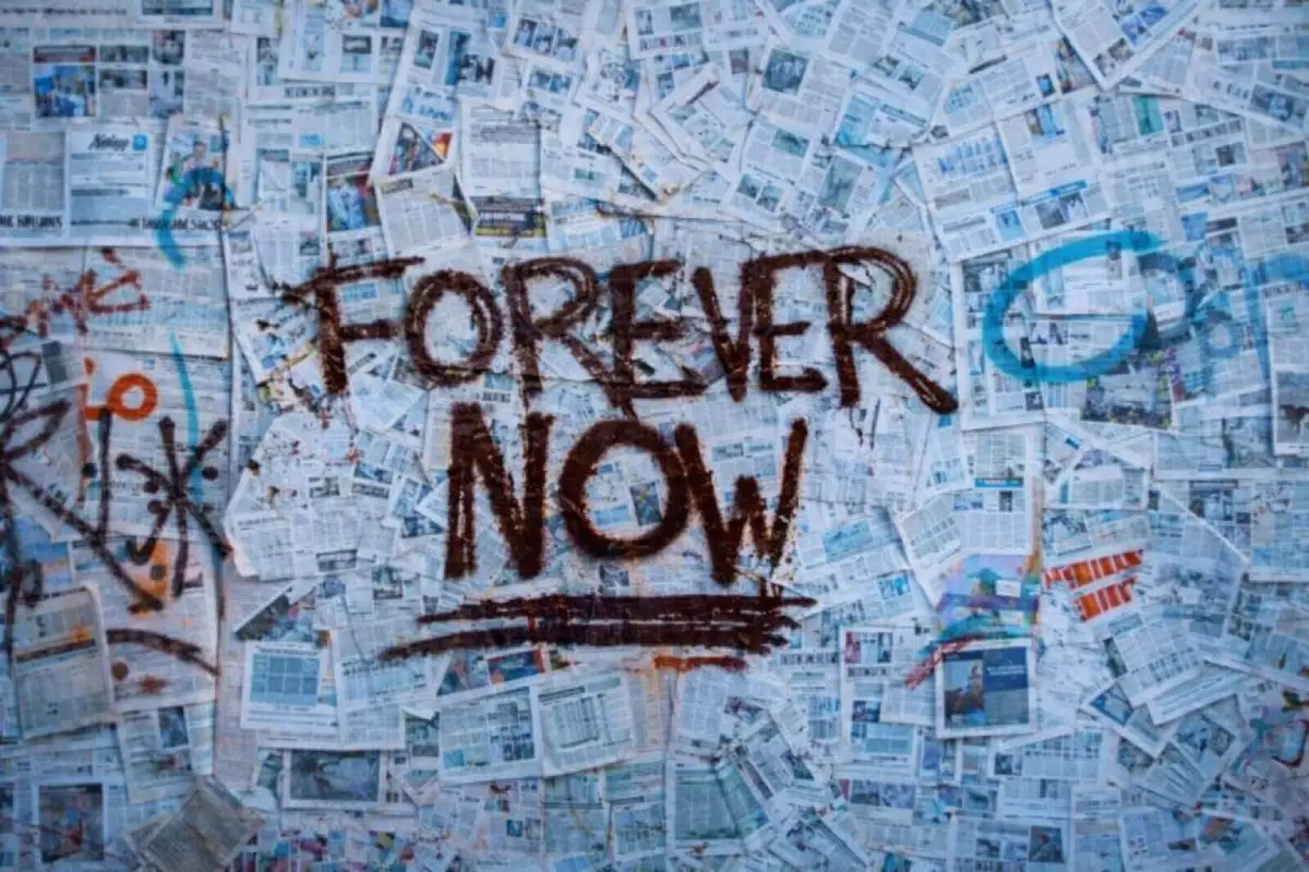 Close-up promotional artwork for Switchfoot’s Forever Now era featuring a wall completely layered with overlapping newspaper pages and print clippings. Across the center, the words “FOREVER NOW” appear hand-painted in dark graffiti-style lettering with an underline, surrounded by scattered spray-painted marks and symbols, creating a collage aesthetic that reflects urgency, reflection, and the album’s present-focused narrative