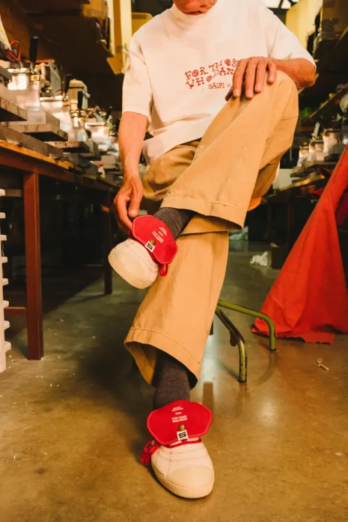 Close-up of the Victoria x SALPI vulcanised boots featuring oversized red overlapping tongues, visible stitching, and layered laces, worn inside a warm-toned footwear factory workspace