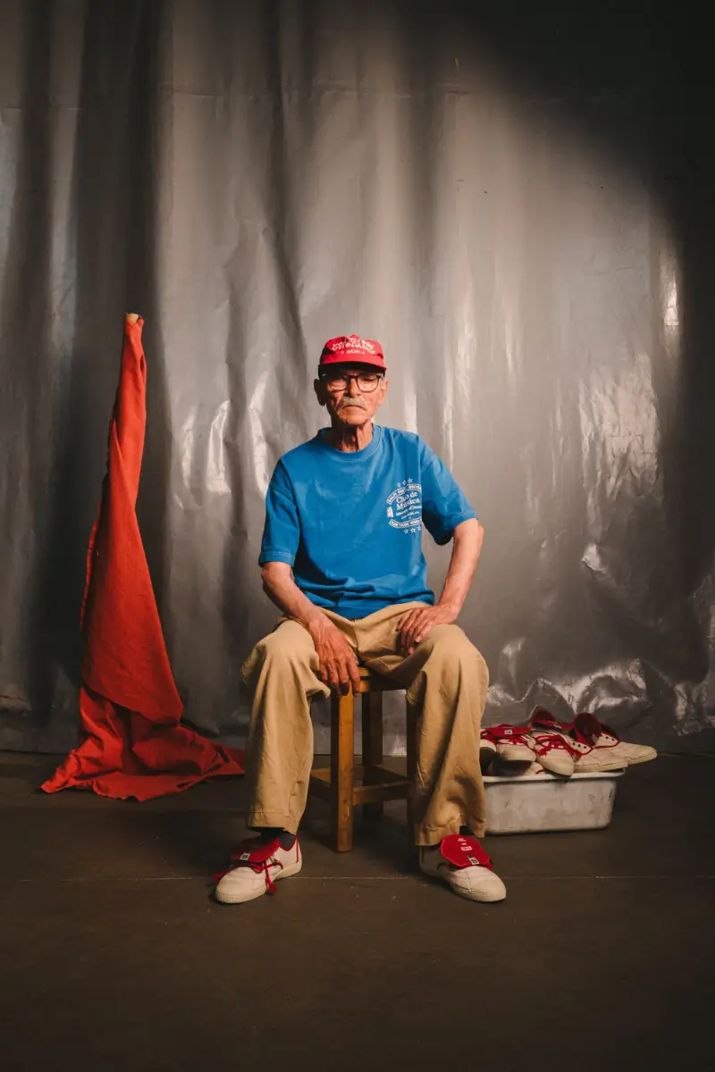 SALPI founder seated in a minimalist studio setting wearing the Victoria x SALPI vulcanised shoe, framed by draped industrial fabric and additional footwear pairs beside him