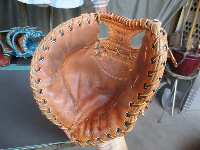 Vintage Wilson first baseman’s mitt in worn tan leather with black lacing, embossed player signature details, and “Triple Lock” branding, photographed in a workshop setting surrounded by classic baseball gloves and equipment