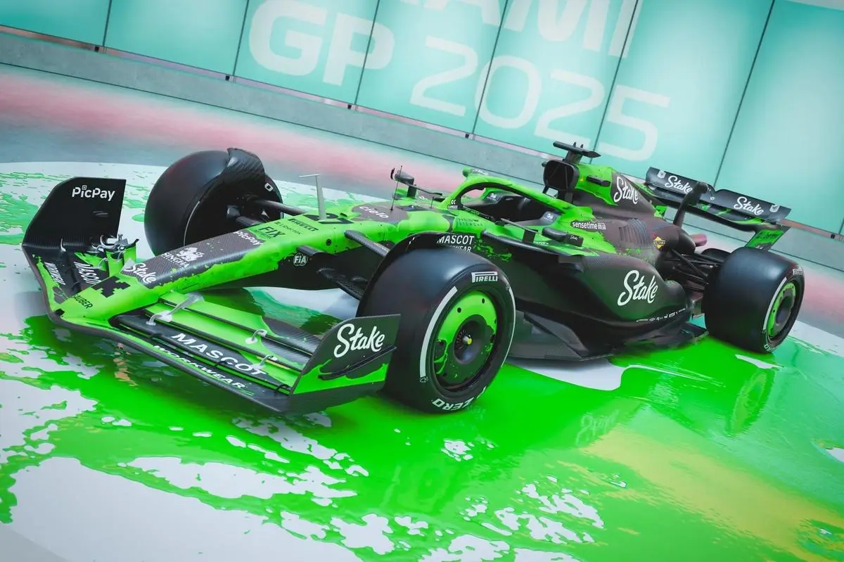 A Formula 1 car is showcased in a striking, high-impact display, finished in a vivid neon green and black livery that appears to spill onto the floor like liquid paint. The car’s bodywork features prominent sponsor branding, including “Stake,” “Mascot Workwear,” and “PicPay,” integrated across the aerodynamic surfaces. Black carbon elements contrast sharply with the electric green accents, while matching green wheel details reinforce the cohesive visual identity. Set against a backdrop reading “Miami GP 2025,” the scene feels like a stylized activation or launch moment rather than a traditional track setting. The reflective floor amplifies the illusion of paint spreading outward from the car, giving the presentation a surreal, almost digital-art quality. The overall composition blends motorsport engineering with experiential design, turning the car into both a performance machine and a visual centerpiece