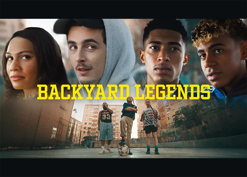 Promotional still from adidas’ “Backyard Legends” campaign featuring a cinematic collage of football personalities and neighborhood players. The image places four close-up portraits across the top — including Trinity Rodman, Timothée Chalamet, Jude Bellingham, and Lamine Yamal — above a gritty urban street football court where three young local “Invincibles” stand around a ball. Bold yellow “BACKYARD LEGENDS” typography dominates the center, while chain-link fences, apartment blocks, and warm cinematic lighting reinforce the nostalgic, grassroots football atmosphere tied to adidas’ 2026 World Cup campaign