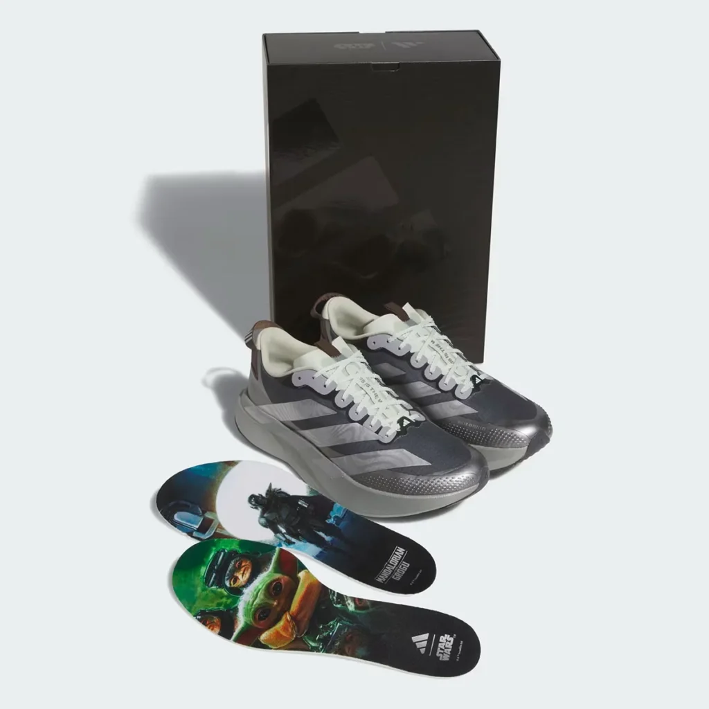 Packaging and accessories shot of the adidas Star Wars Mandalorian & Grogu Adizero EVO SL ATR featuring the special-edition shoebox, dual character graphic insoles with Din Djarin and Grogu artwork, and the full performance runner presented in its cinematic collector-focused configuration