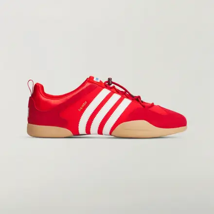 Side profile product image of the Bad Bunny x adidas Ballerina sneaker in vivid red, featuring tonal laces, signature white Three Stripes branding, a low-profile silhouette, and a gum rubber outsole set against a clean light grey background