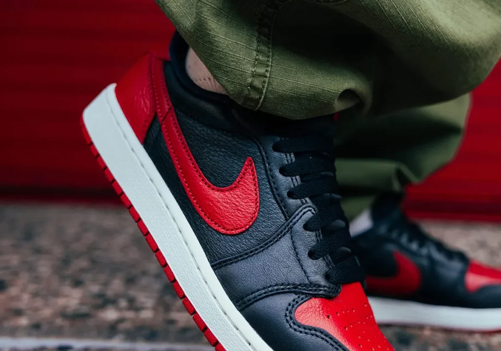 On-foot side view of the Air Jordan 1 Low OG “Banned” featuring black leather panels, textured varsity red Swoosh, white midsole, and red outsole