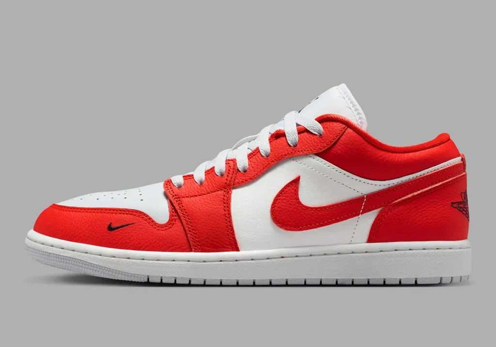 Full lateral side profile of the low-top shoe dressed in a vibrant chile red and white palette. Rich textured red leather overlays dominate the mudguard, eyestays, Swoosh, collar, and heel, contrasted against smooth white leather quarter panels and toe sections. White flat laces and a clean white midsole enhance the crisp two-tone presentation, while a miniature black Swoosh near the forefoot and a partially visible black Wings logo at the heel introduce subtle contrast details. The overall construction channels classic Air Jordan heritage with a bold contemporary finish