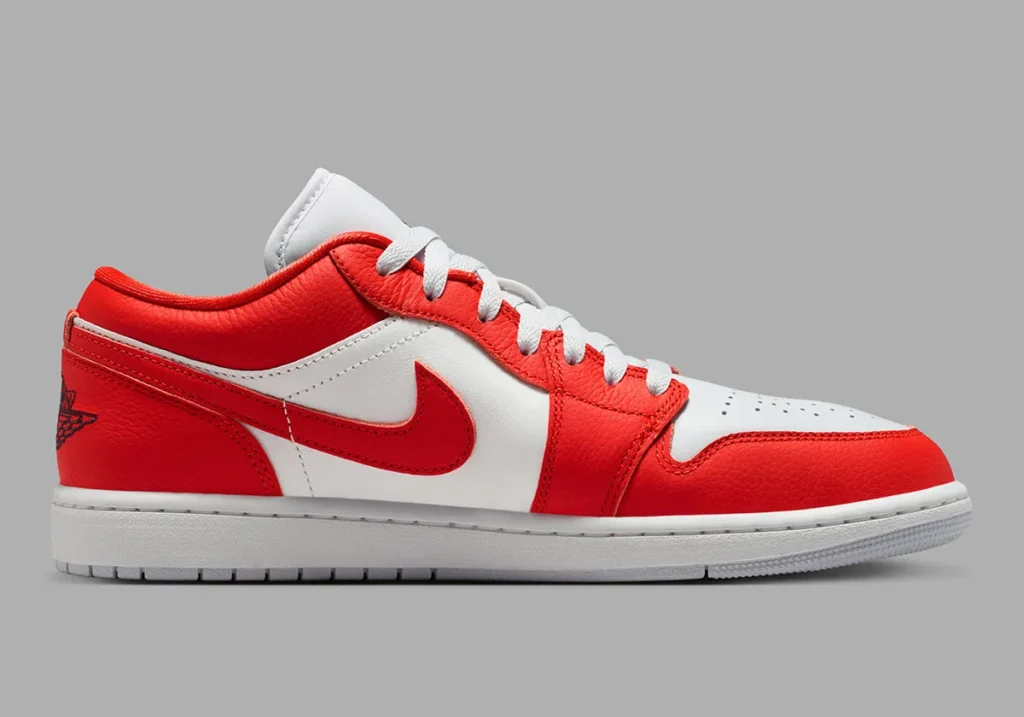 Clean lateral profile shot of the low-top shoe revealing its striking chile red and white color-blocked construction. Textured red leather overlays wrap around the mudguard, eyestays, heel, and collar, layered over smooth white leather side panels and toe sections. A matching red leather Swoosh stretches across the midfoot, while white laces, a crisp white midsole, and a light grey outsole maintain the silhouette’s classic retro basketball aesthetic. The black embroidered Wings logo at the heel adds a subtle contrast detail against the vivid red rear panel