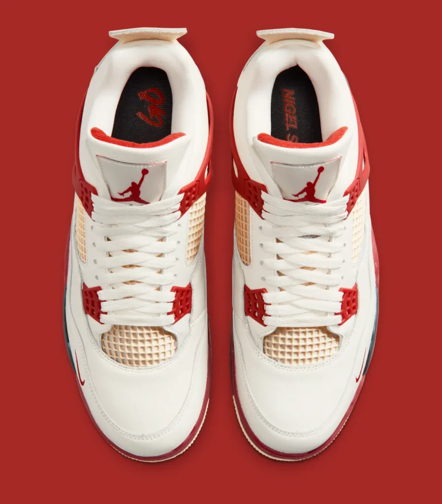 A top-down studio image of the Air Jordan 4 “Brick by Brick” displayed symmetrically against a rich red background. The shoe feature an off-white leather construction with cream-toned mesh netting across the tongue and toe box, complemented by bright red TPU lace wings and eyelets that frame the lacing system. White flat laces run through the center, leading to tongue patches embroidered with matching red Jumpman logos. The interior lining introduces a vivid red accent around the collar, while the black insoles carry contrasting red graphic branding and lettering. The composition highlights the Jordan 4’s layered panel construction, geometric cage detailing, and vintage-inspired cream finish throughout the upper