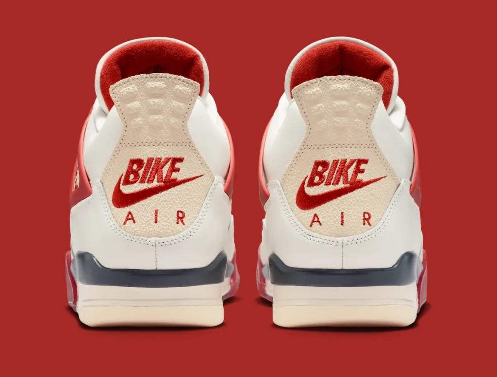 A rear-facing studio image of the Air Jordan 4 “Brick by Brick” shown against a bold red backdrop, emphasizing the sneaker’s vintage-inspired heel construction. The off-white leather upper transitions into textured cream heel tabs embroidered with oversized red Nike Air branding, delivering a classic retro basketball aesthetic. Soft red interior lining wraps around the collar, adding contrast to the otherwise neutral upper palette. Dark navy detailing spans the rear portion of the midsole above visible Air cushioning units, while translucent red outsole accents subtly appear along the heel edges. The image highlights the Jordan 4’s sculpted back profile, heritage Nike Air treatment, and layered material mix that combines aged textures with bold archival tincture blocking