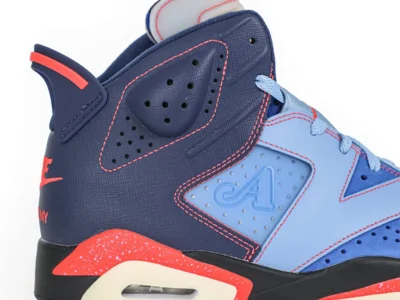 Side profile detail of the collection Jordan Brand Air Jordan 6 x Awake NY sneaker, emphasizing the layered contrast between midnight navy textured panels and light blue leather overlays. Infrared-red stitching sharply outlines the sculpted geometric construction, while the embossed Awake NY “A” logo appears within the perforated side panel insert. The speckled infrared midsole wedge, visible Air unit, translucent cream outsole, and signature spoiler-inspired heel tab reinforce the shoe iconic early-1990s basketball heritage, blending archival Air Jordan performance design with modern New York streetwear aesthetics