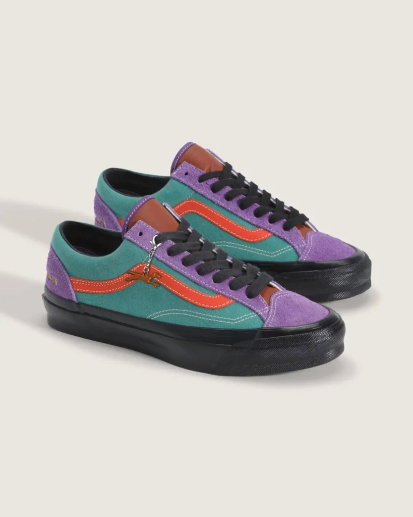 Vibrant OTW by Vans Old Skool shoe featuring teal canvas uppers, lavender suede overlays, orange side stripes, black laces and sole unit, accented with contrast stitching and a dangling metallic charm in a playful retro-inspired color palette against a neutral studio background