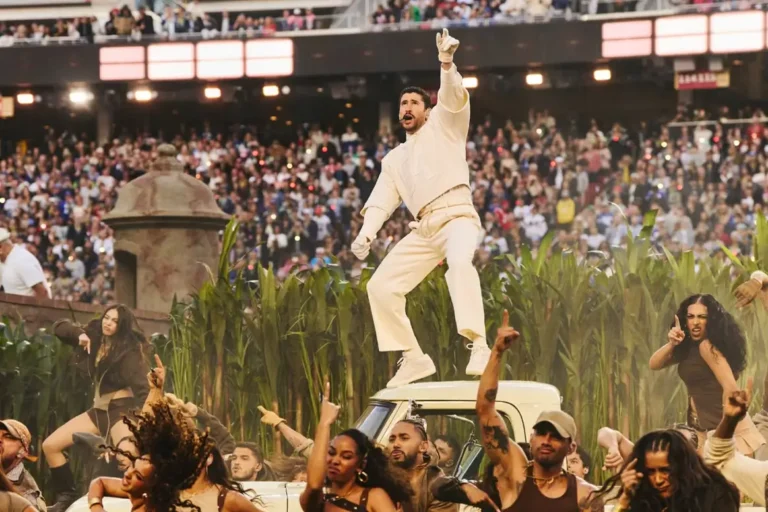 Bad Bunny performs during the Apple Music Super Bowl LX Halftime Show wearing a monochromatic cream Zara ensemble while standing atop a vintage car surrounded by dancers, lush tropical staging, and a packed stadium crowd celebrating Puerto Rican culture and high-energy performance spectacle