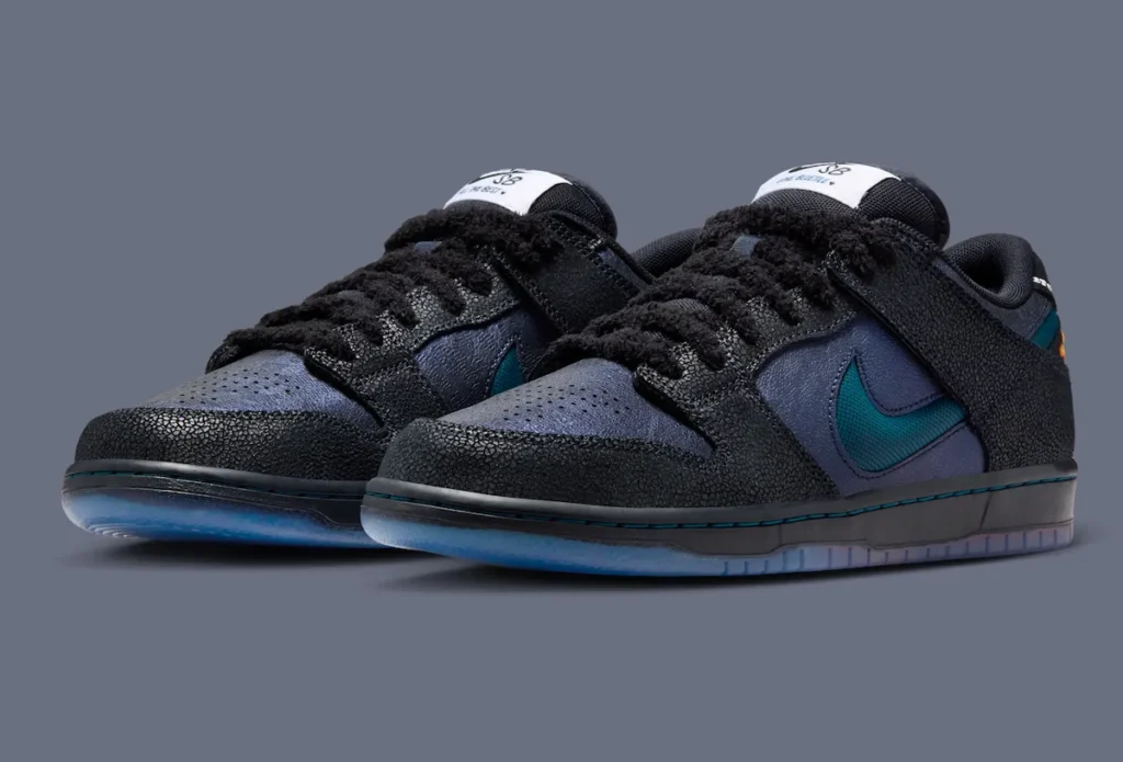 Pair of the Bluetile x Nike SB Dunk Low “Monarch Butterfly” shoe featuring cracked black textured overlays, shimmering navy leather uppers, fuzzy black laces, deep Marina blue Swooshes, and translucent gradient outsoles inspired by South Carolina sunset tones